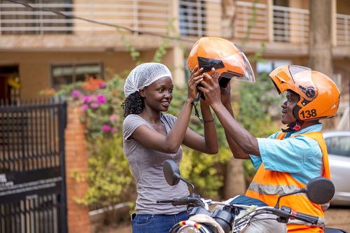 SafeBoda increased trip costs A SafeBoda rider helps a passenger wear a helmet (Image courtesy via xtra-ordinary)
