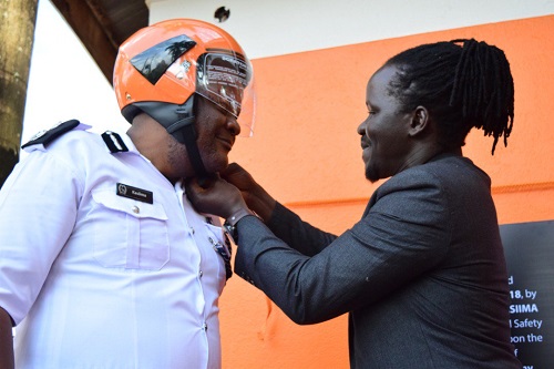 SafeBoda co-founder Ricky Thompson helps the head of traffic Dr. Steven Kasiima wear a helmet at the launch of the SafeBoda Academy (Pictured by Young Achievers Awards)